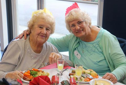 Two elderly women smiling over table of food